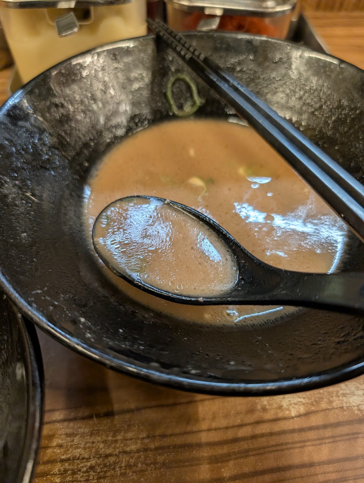 食べ終えた黒い丼の底に残る豚骨醤油スープと黒い箸・レンゲのクローズアップ